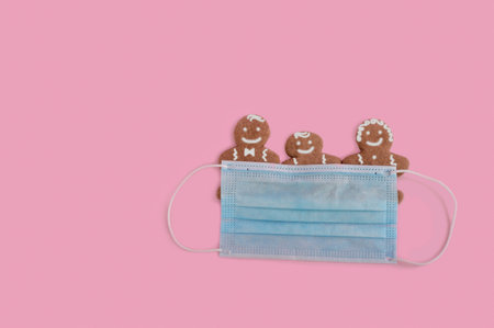 Three gingerbread cookies covered with a face mask on a pastel pink background - pandemic conceptの写真素材