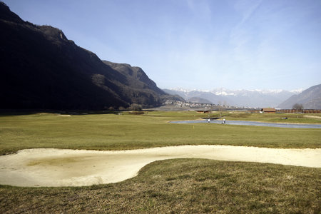 A wide shot of a beautiful blue monster golf course in South Tyrol, Italy surrounded by mountains and a clear blue sky in the backgroundの写真素材