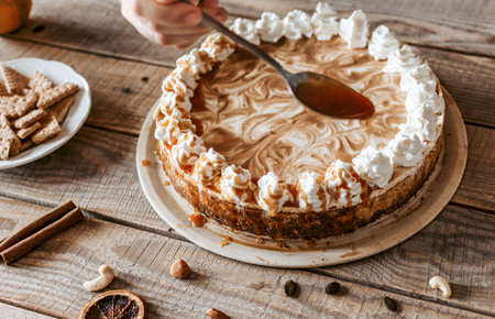 A closeup of female hands covering a yummy pumpkin cheesecake with a syrup, other ingredients on the tableの写真素材