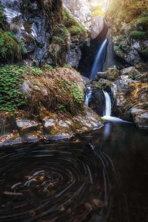 A vertical shot of a waterfall into a pond surrounded by cliffsの写真素材