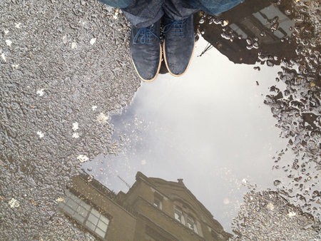The man standing near the rainwater on the ground in the street reflecting the sky and a buildingの写真素材