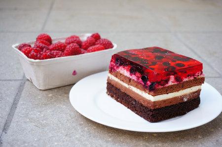 A closeup shot of raspberries in a plastic container next to a raspberry cake piece