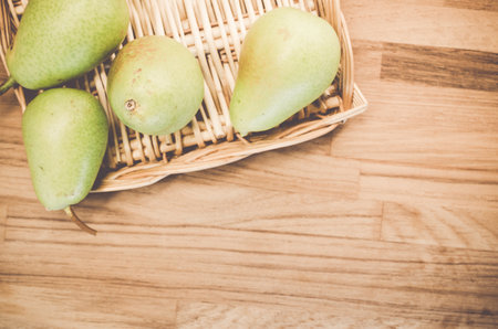 A top view of some green pears on a wicker basket and wooden surfaceの写真素材