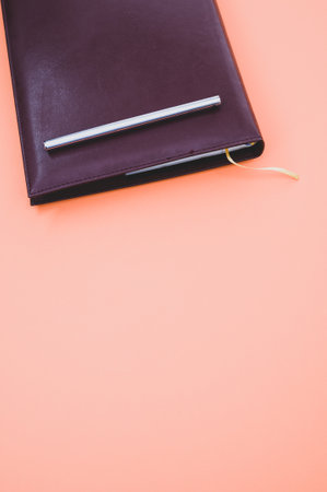 A top view closeup of a black notebook with a yellow bookmark and a pen isolated on an orange backgroundの写真素材