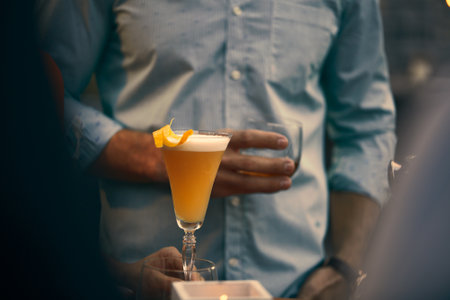 A closeup shot of a beautiful yellow cocktail and a person holding a glass of whiskeyの写真素材