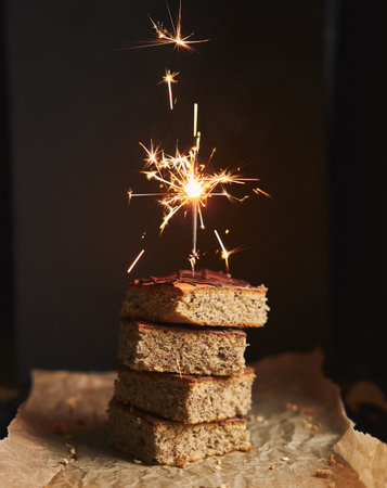 A vertical shot of a pile of delicious nut cakes with chocolate glaze and sparkle on the top with a black blurred backgroundの写真素材