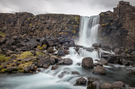 The Oxararfoss waterfall in Thingvellir, Iceland under a clouded skyの写真素材