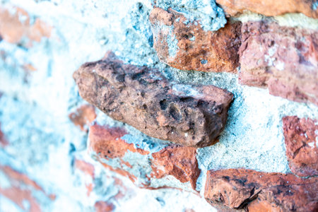 A brick wall with white mortar, with the bricks, standing out of the wall unevenly and broken