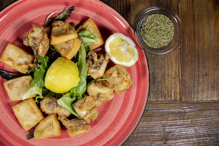 An overhead shot  red plate with fried cuttlefish, spices and salt, rustic wooden background