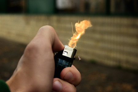 A closeup selective focus shot a man lighting a lighter with buildings on the background