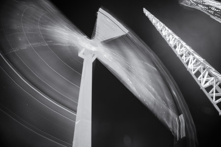 A greyscale low angle long exposure shot of a windmill and construction at nightの写真素材