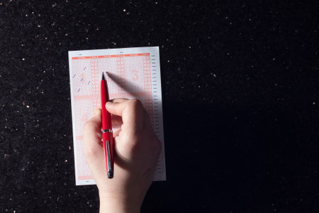 A person's hand filling in the checklists in a planner on a black surface