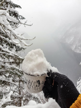 A closeup of a person holding a cup full of snow with gloves on the frozen lake backgroundの写真素材