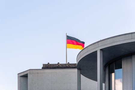 The flag of Germany on a pole flying over a building in Berlin, Germany against a cloudy skyの写真素材