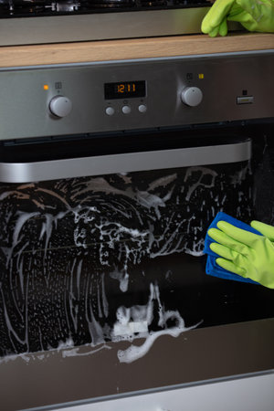 A closeup of a person with gloves disinfecting the oven under the lights - coronavirus concept