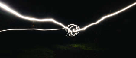 A dark abstract background with white motion paint lights on grass field