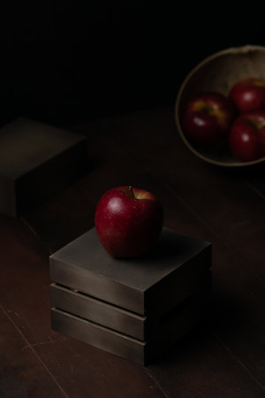 A vertical shot of a ripe red apple on a small wooden box on the table with a dark blurry backgroundの写真素材