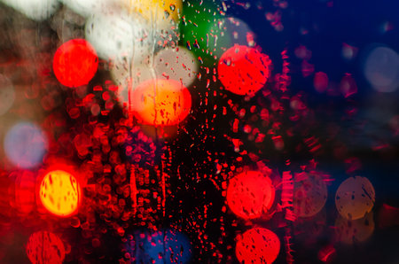 The colorful night bokeh lights on the window with raindrops
