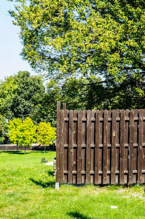 A vertical image of a wooden fence with green lawn and trees