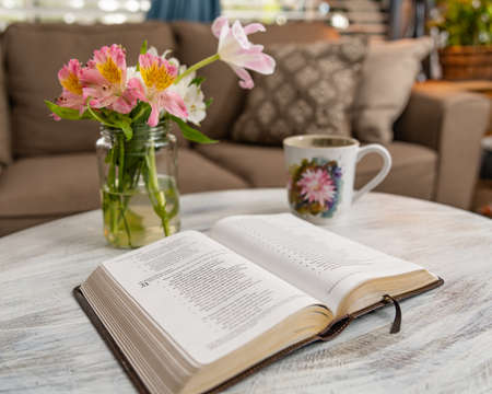 A closeup shot of an open book on a table with flowers and a mug nearby