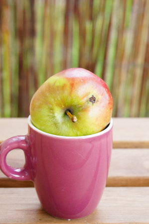 A vertical closeup shot of fresh apple in a cup on a wooden tableの写真素材