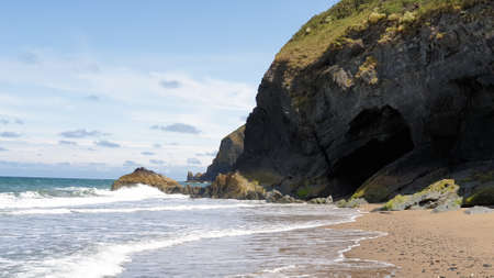 A beautiful shot of caves with greenery on the hill on a sandy shore near an oceanの写真素材