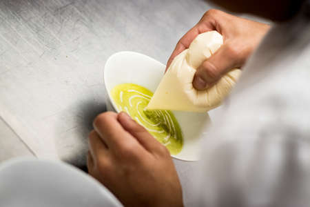 A closeup shot of a chief adding white cream in a green vegan soupの写真素材
