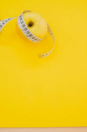 An apple with measuring tape isolated on yellow backgroundの写真素材