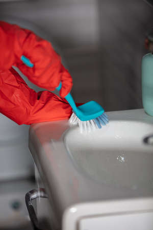 A person cleaning the sink with a blue cleaning brush