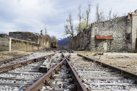 An area with train tracks surrounded by old concrete buildings under a cloudy sky