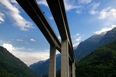 A low angle view of a concrete bridge surrounded by hills covered in forests under the sunlightの写真素材