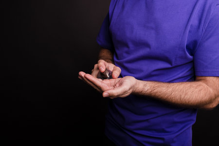 A closeup of a man using a hand sanitiser against a black background - COVID-19の写真素材