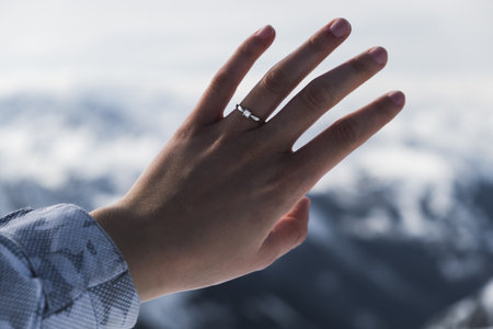 A closeup shot of a hand of a woman wearing a ring in front of the mountainの写真素材