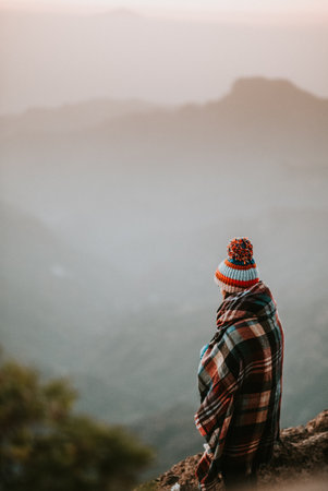 A vertical shot of a girl wearing a hat and sitting on a mountain