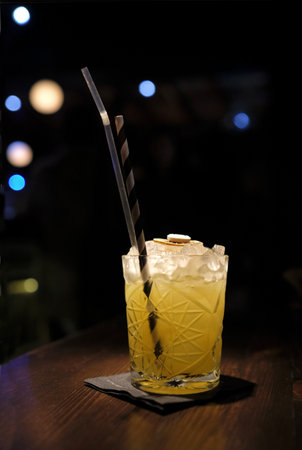 A vertical shot of a yellow cocktail with a straw on a wooden table