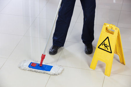 A person cleaning the floor with a flat mop near a yellow caution wet floor sign