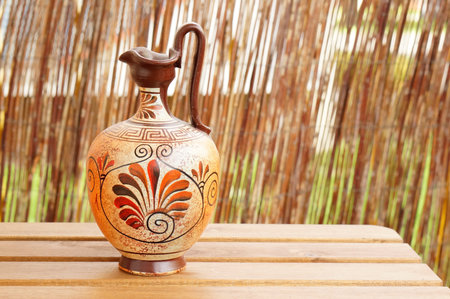 A closeup shot of a Greek vase on a wooden table with a blurry backgroundの写真素材