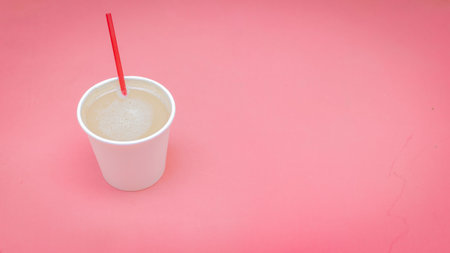 A closeup shot of a white paper cup filled with coffee with milk on a pink backgroundの写真素材