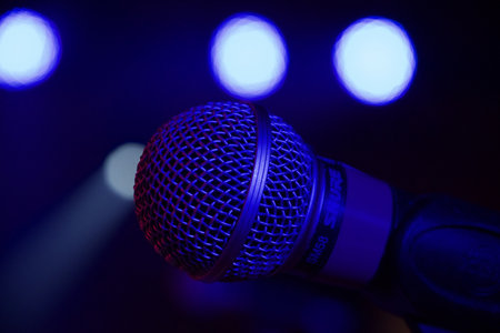 A closeup shot of a microphone set on a stage during an event with lights in the backgroundの写真素材