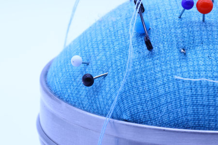 Multicolored sewing and safety pins stuck on a blue pillowの写真素材