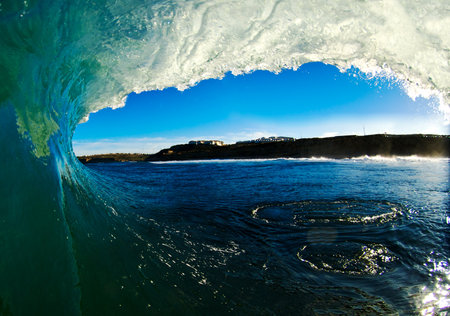 A view of a cliff shoreline and blie sky through a wave in the ocean