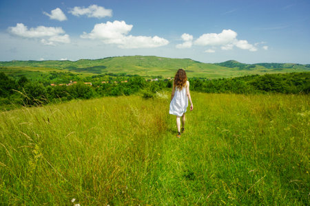 A wide shot of a young woman in a dress walking in a grassy field on a cool and cloudy dayの写真素材
