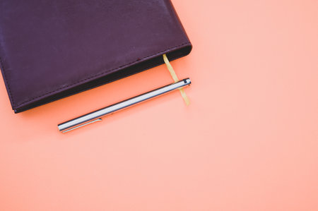 A top view closeup of a black notebook with a yellow bookmark and a pen isolated on an orange...