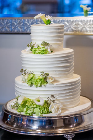 A vertical shot of a three-layered white cake with flower decorationsの写真素材