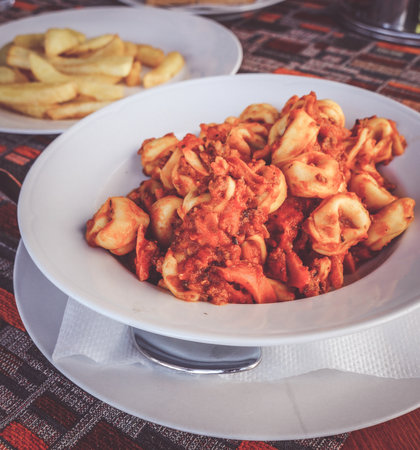 Fresh tortellini with tomato sauce served in a white plate on a table.の写真素材