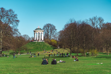 MUNICH, GERMANY - Mar 08, 2020: Friends sitting in the English Garden (Englischer Garten) in Munich on a beautiful sunny day in winter. Monopterus in the backgroundのeditorial素材