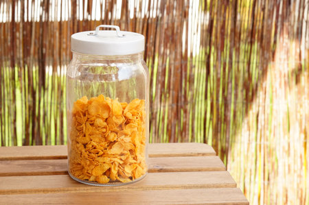 A glass jar filled with corn flakes on a wooden table