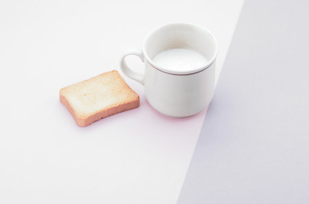 A high angle shot of fresh milk on a cup with bread on a pink surfaceの写真素材