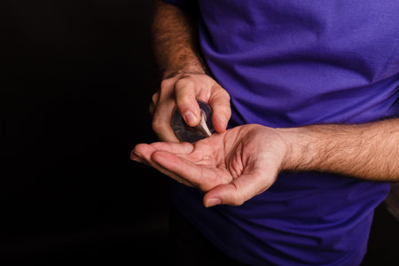 A closeup of a man using a hand sanitizer against a black backgroundの写真素材