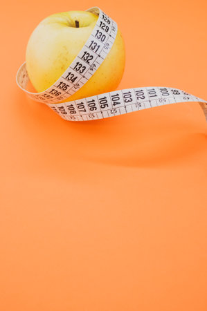 An apple with measuring tape isolated on orange backgroundの写真素材